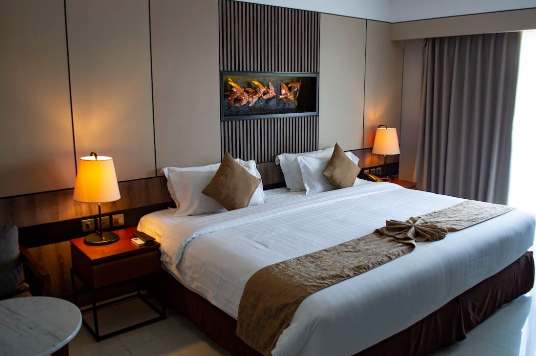 A hotel room with a large bed, two nightstands with lamps, and a fireplace on the wall.
