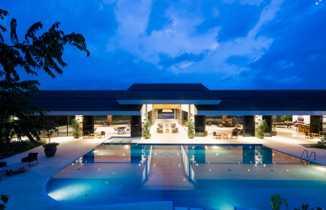A nighttime view of a hotel pool area with a large pool, lounge chairs, and a building in the background.