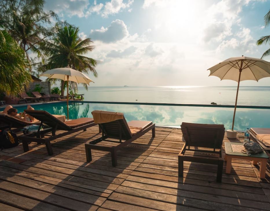 A poolside deck with lounge chairs, umbrellas, and a view of the ocean