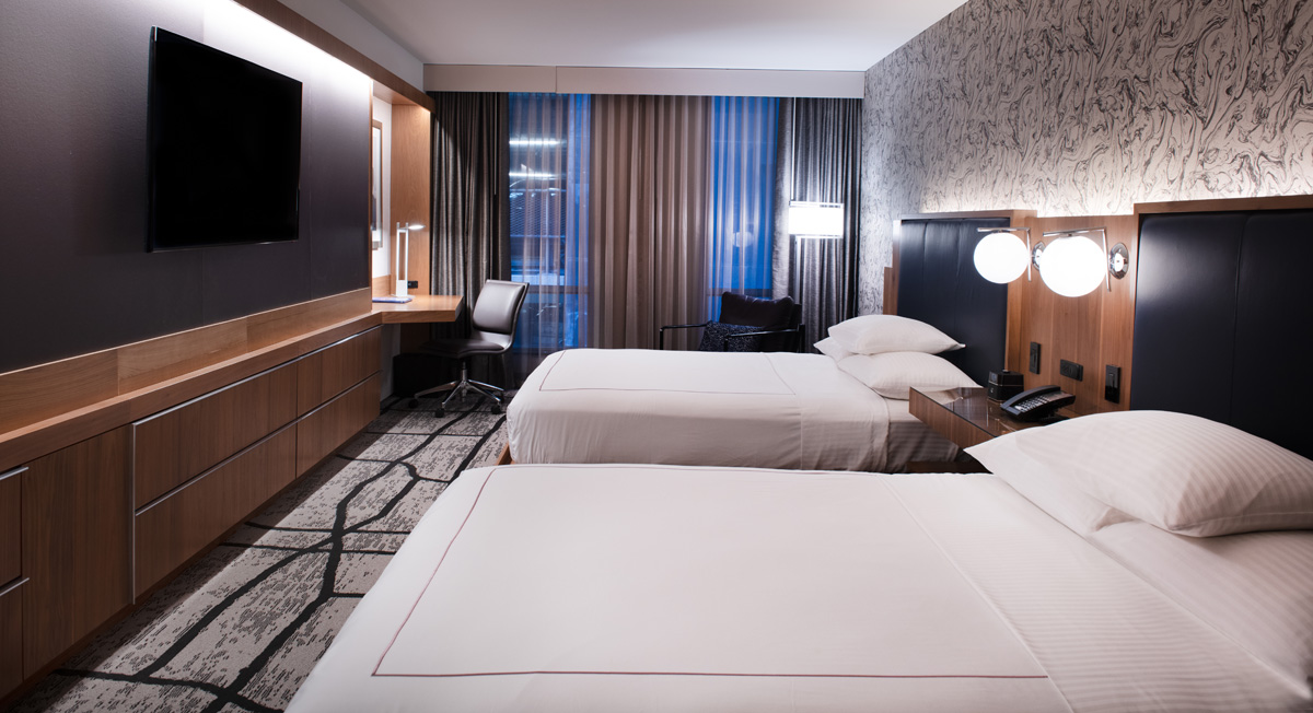 A hotel room with two twin beds, a desk, TV, and window with curtains.